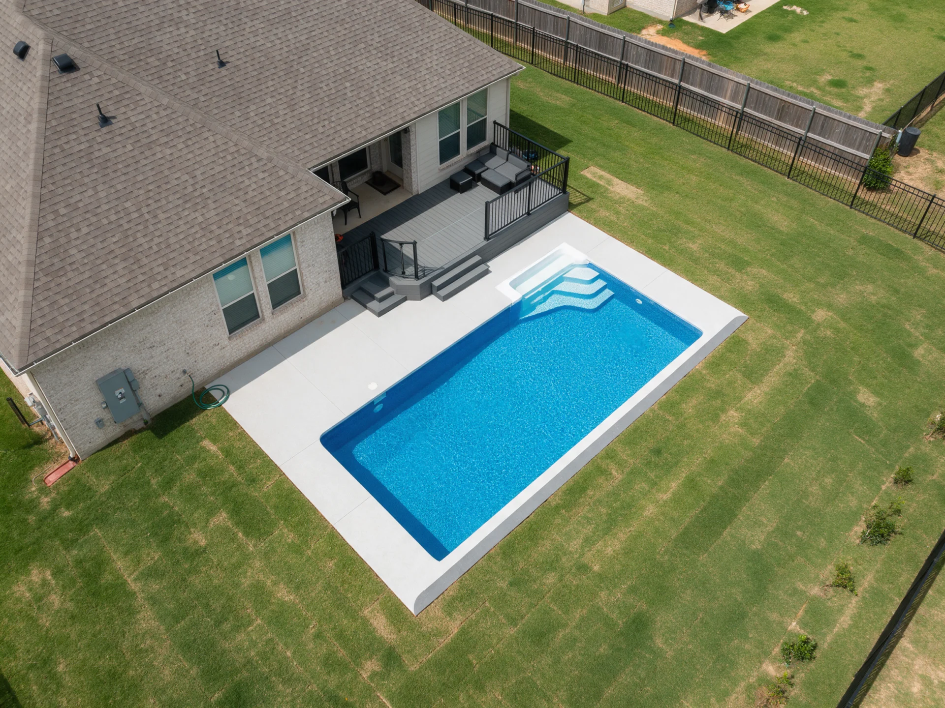 Illustrative image: Aerial drone view of a residential backyard with a new in-ground swimming pool and pool deck next to